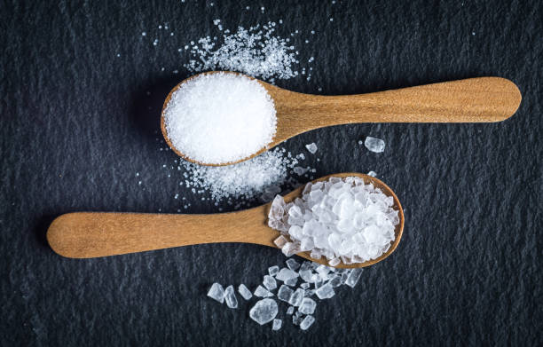 Different types of salt. Top view on two wooden spoons Different types of salt. Sea and kitchen salt. Top view on two wooden spoons on black background salt mineral photos stock pictures, royalty-free photos & images