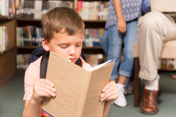 istock Caucasian little boy reading books in school library. 922912730