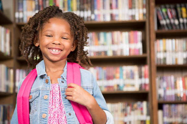 istock African descent little girl in school library with book. 922917536