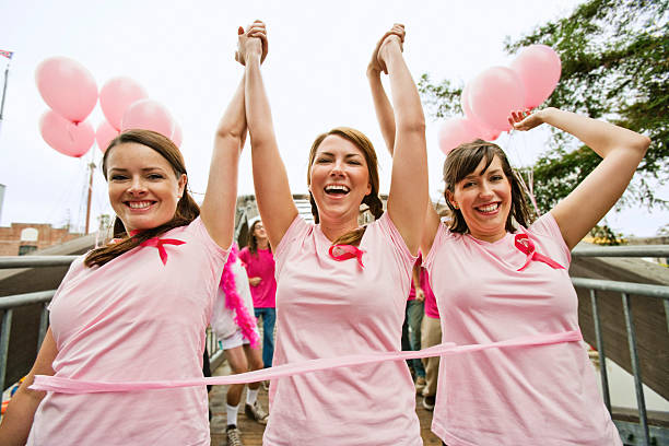 Women run in breast cancer marathon Three young women dressed in pink run in marathon to fight breast cancer. They joyfully cross the finish line at the end of a bridge with pink balloons. petaluma stock pictures, royalty-free photos & images