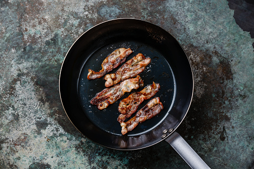 Fried bacon in frying cooking pan on metal background