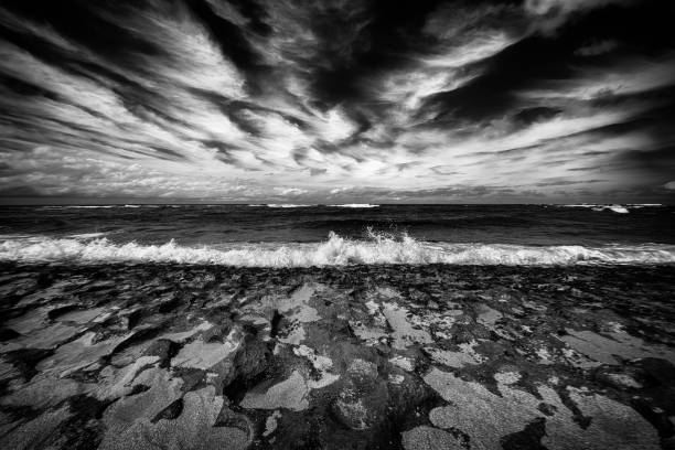 The clouds forming a pattern over a volcanic rock layered beach on Oahu, Hawaii in black and white.