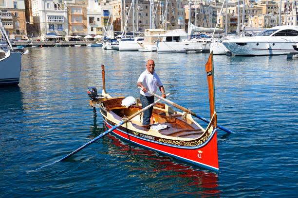 Man steering a Dghajsa boat, Malta. Man steering a traditional Maltese Dghajsa water taxi in the harbour with views towards Senglea waterfront, Vittoriosa, Malta, Europe. coconut crab stock pictures, royalty-free photos & images