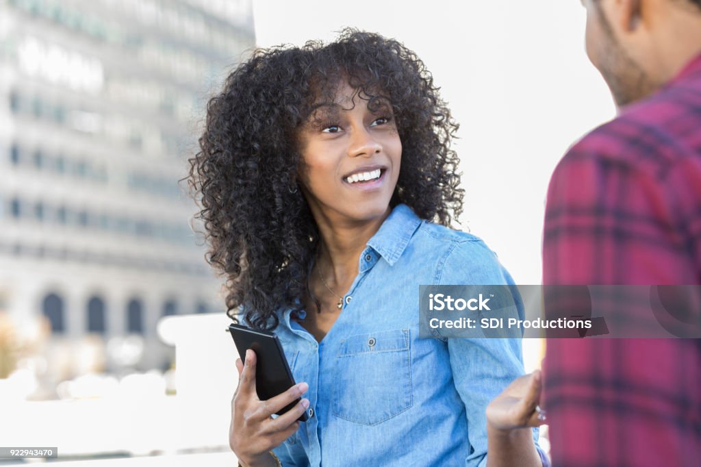 Young woman runs into old friend on city street A surprised young woman pauses from texting on her smart phone to greet an unrecognizable old friend on a city street. Stranger Stock Photo