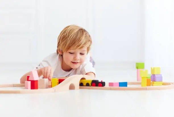 Photo of cute kid playing with toy railway at home