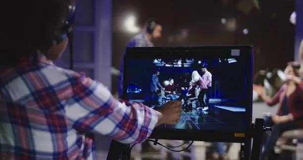 Casual African-American woman in headset controlling process of shooting TV show standing in front of computer screen and watching record.