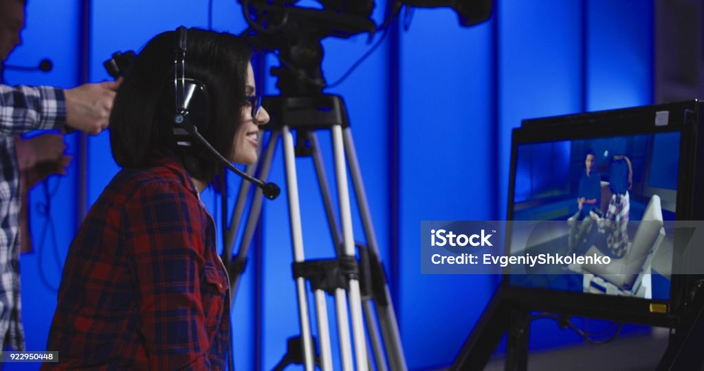 Woman giving instructions in a newsroom Woman wearing a headset sitting behind a monitor with the cameraman during production giving instructions in a newsroom gesturing and pointing Movie Stock Photo