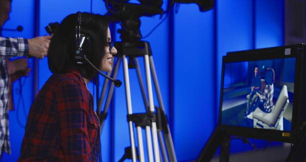 Woman giving instructions in a newsroom Woman wearing a headset sitting behind a monitor with the cameraman during production giving instructions in a newsroom gesturing and pointing crew photos stock pictures, royalty-free photos & images