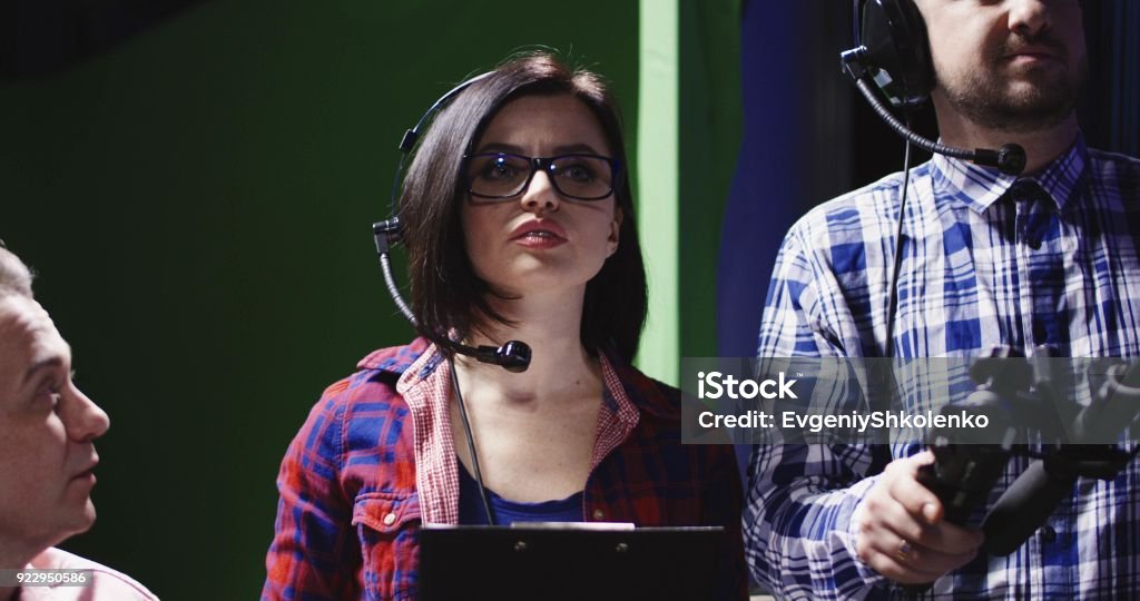 Female producer or prompt wearing a headset Female producer or prompt wearing a headset and holding a clipboard alongside a cameraman in a production studio panning to male colleague on the left of the screen. Producer Stock Photo