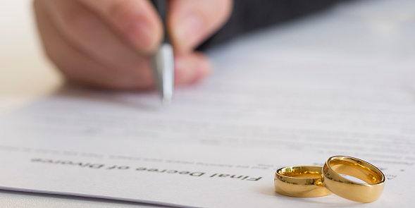 Hands of wife, husband signing decree of divorce, dissolution, canceling marriage, legal separation documents, filing divorce papers or premarital agreement prepared by lawyer. Wedding ring.