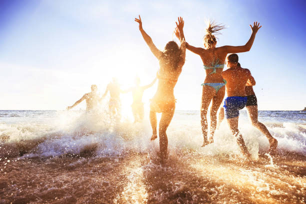 Happy friends at sunset sea beach Big crowd of friends having fun at sunset sea beach. Beach vacations concept jumping teenager fun group of people stock pictures, royalty-free photos & images