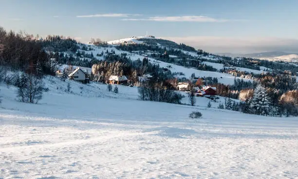 nice landscape of winter Silesian Beskids mountains with dispersed settlement of Koniakow village, Ochodzita hill, snow and blue sky with clouds in Poland
