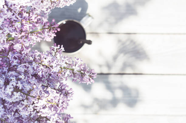 A metal mug with coffee and lilac branches on a wooden table