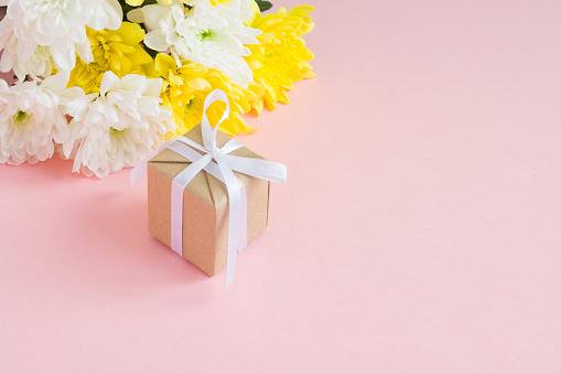 March 8 Women's Day card. Bouquet of white and yellow chrysanthemums and gift on a pale pink background