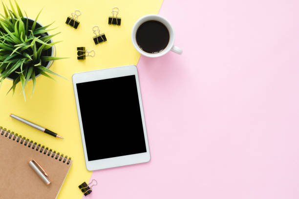istock Office desk working space - Flat lay top view photo of working space with blank mock up tablet, coffee cup and notebook on pastel background. Pastel pink yellow color copy space working desk concept. 922988972