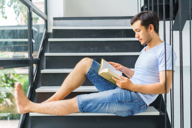 istock Handsome man reading book on stairs at home. concept of knowledge examination