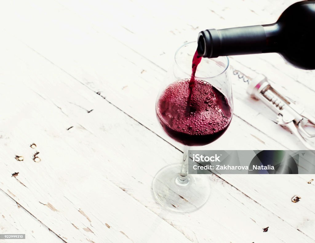 Versando vino rosso dalla bottiglia in bicchiere di vino su tavolo in legno bianco vintage con spazio di copia. - Foto stock royalty-free di Vino
