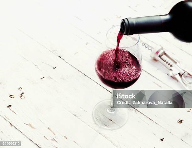 Pouring Red Wine From Bottle In Wine Glass On Vintage White Wooden Table With Copyspace Stock Photo - Download Image Now