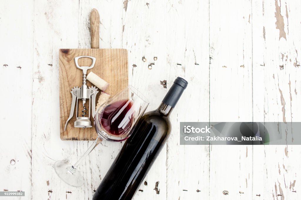 Una copa de vino tinto, botella, sacacorchos y corchos de vino a bordo rústico sobre mesa de madera blanca, copyspsce. Concepto «n la degustación - Foto de stock de Vino libre de derechos