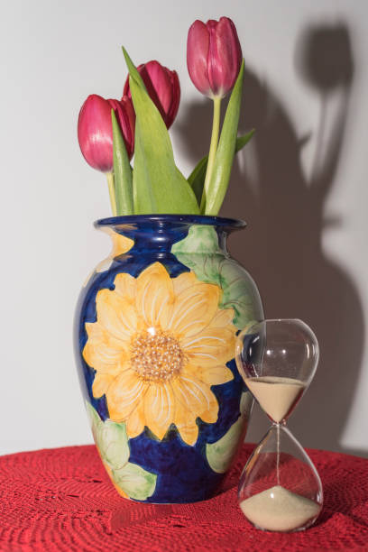 red tulips in blue ceramic vase of vietri sul mare on red crochet doily and hourglass with sand. - 6206 imagens e fotografias de stock