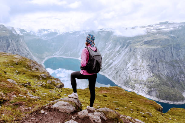 istock Young woman with backpack standing on fjord coast 923007024