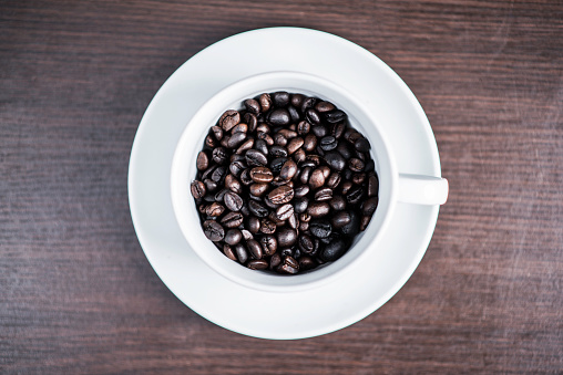 Coffee bean in white cup on wood background.