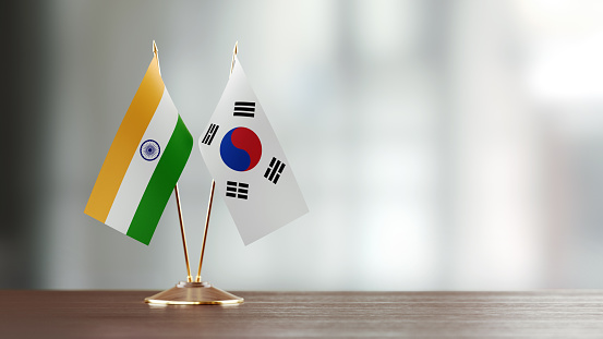 Indian and South Korean flag pair on desk over defocused background. Horizontal composition with copy space and selective focus.