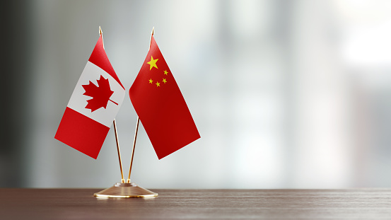 Canadian and Chinese flag pair on desk over defocused background. Horizontal composition with copy space and selective focus.
