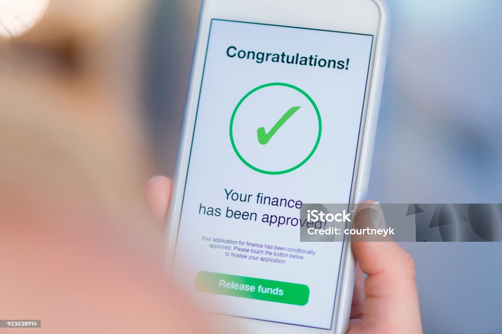 Mortgage Loan approval on mobile phone in a house. Mortgage Loan approval on mobile phone in a house. There is a message on the screen saying her loan in approved. Close up with Copy space Financial Loan Stock Photo