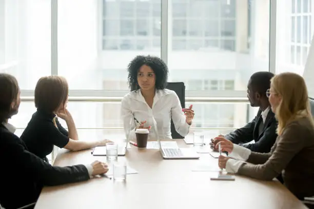 Photo of Black female boss leading corporate meeting talking to diverse businesspeople