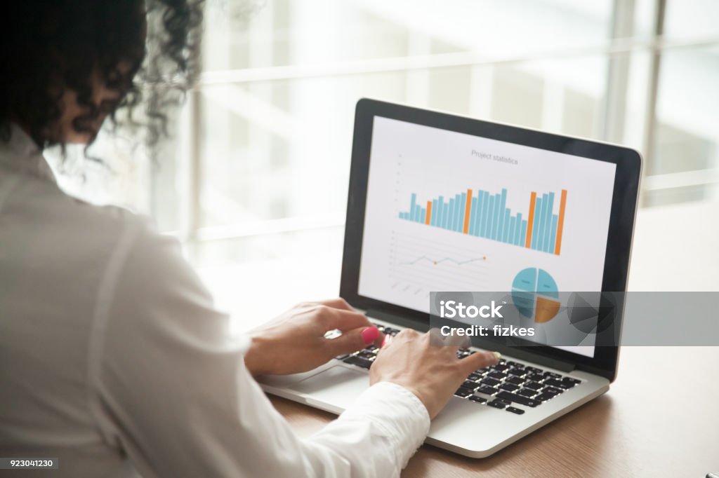 African businesswoman analyzing project statistics on laptop screen, close up African businesswoman analyzing statistics on laptop screen, working with financial graphs charts online, using business software for data analysis and project management concept, rear close up view Computer Monitor Stock Photo