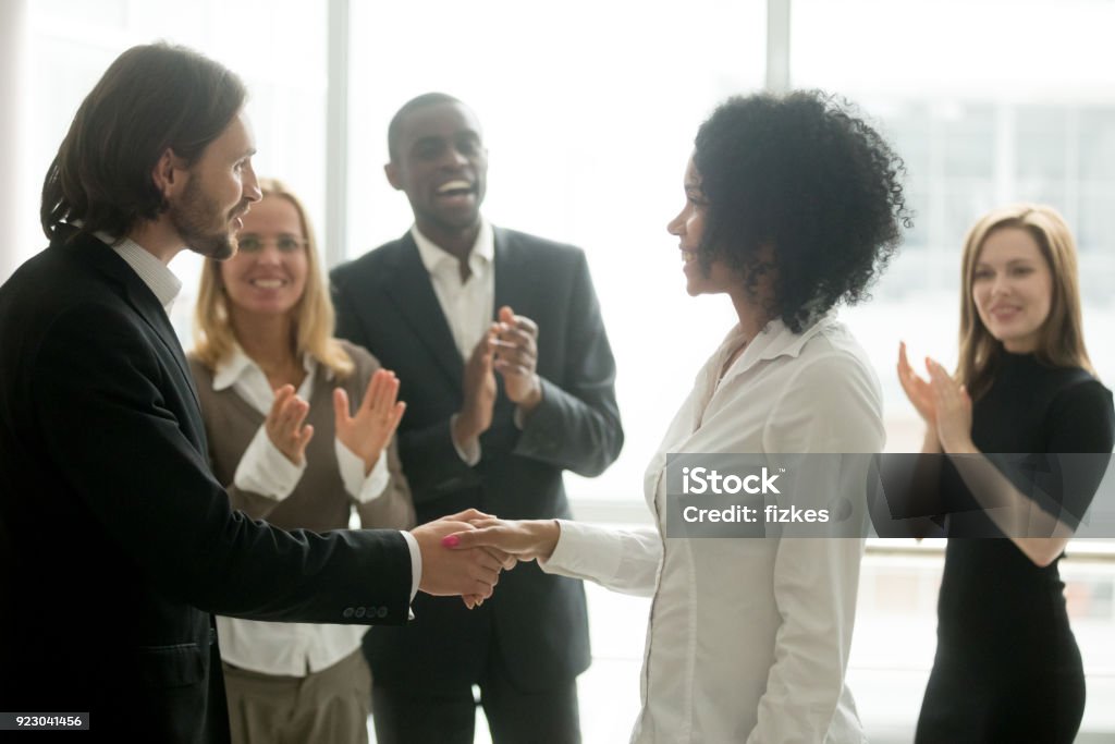 Grateful boss handshaking promoting african businesswoman congratulating with career achievement Grateful boss handshaking promoting african businesswoman congratulating with career achievement while colleagues applauding cheering successful worker, appreciation handshake, employee recognition Ladder of Success Stock Photo