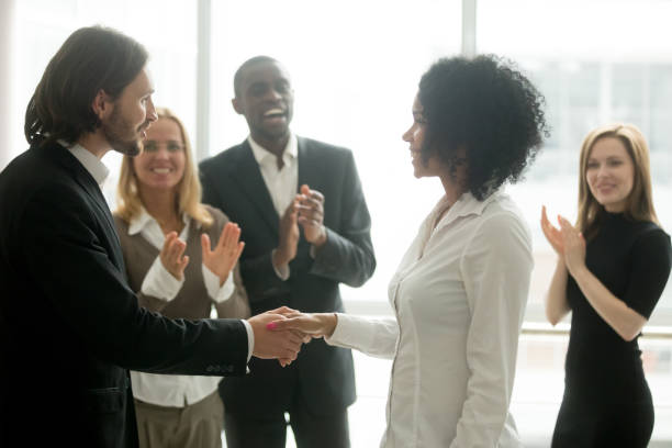 Grateful boss handshaking promoting african businesswoman congratulating with career achievement Grateful boss handshaking promoting african businesswoman congratulating with career achievement while colleagues applauding cheering successful worker, appreciation handshake, employee recognition ladder of success stock pictures, royalty-free photos & images