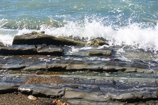 rocky sea shore with pebble beach, transparent waves with foam, on a warm summer day