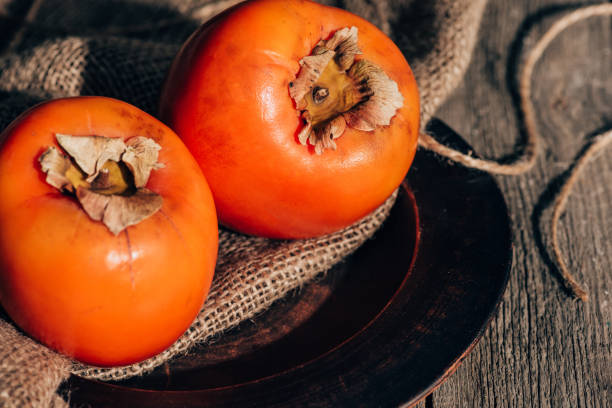 istock two ripe persimmons on sackcloth on wooden table 923079806