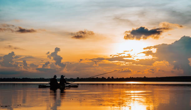 Casal maturo silhueta, Lago de pesca no pôr do sol - foto de acervo