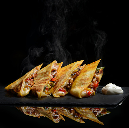 Mexican Quesadilla wrap with chicken   sweet pepper sour cream and salsa hot with steam smoke on black background