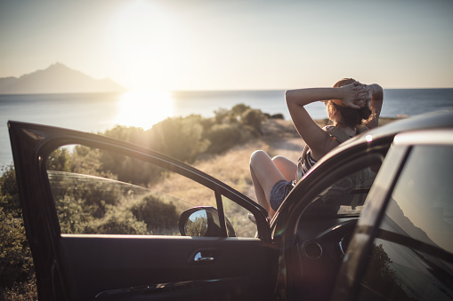 Woman relaxing on her car at the road trip