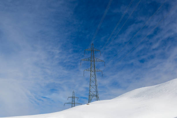 two electricity pylons in winter, white snow, sunny blue sky, clouds
