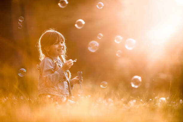 istock Happy girl having fun while blowing bubbles during spring day in grass. 923185180