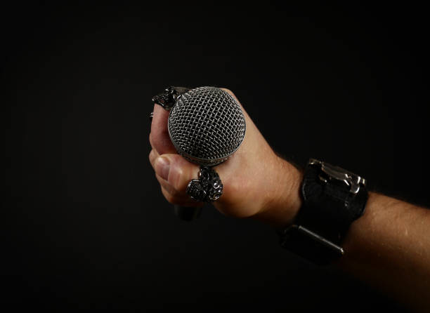 istock Cropped Hand Holding Microphone Against Black Background 923205400