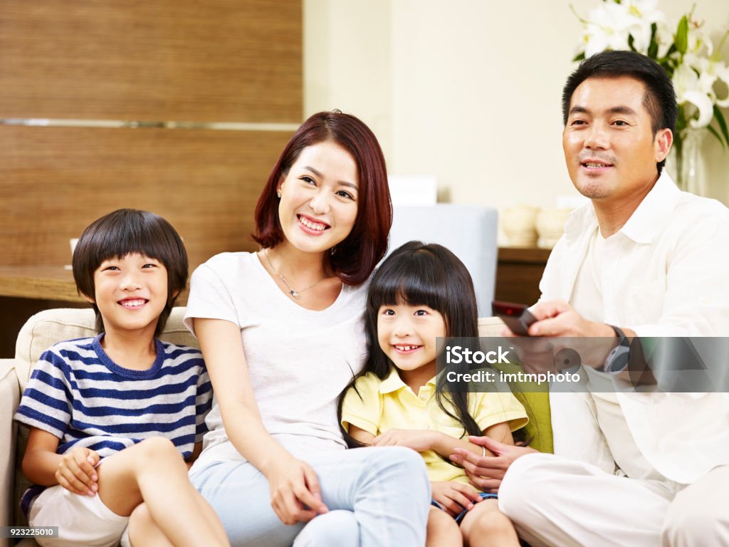 asian family watching TV together at home happy asian family with two children sitting on couch at home watching TV. East Asian Ethnicity Stock Photo