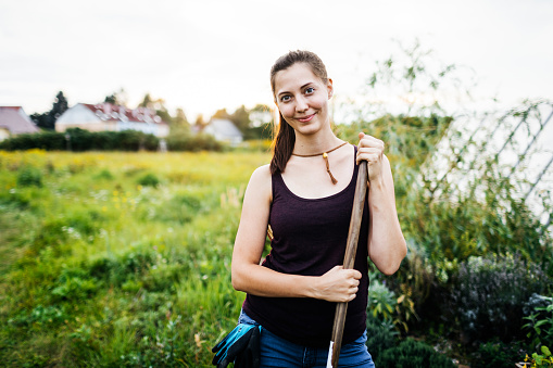 A young urban farmer holding a tool,  smiling after a hard day working.