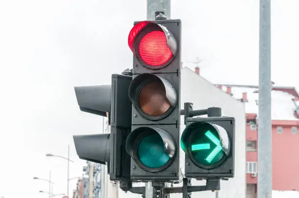 Close up of traffic light on the crossroad with red light for straight direction but green arrow for right turn only in the cold winter day with cloudy sky