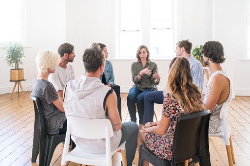 Support group gathering for a meeting. Young woman discussing with people at entrance hall. Males and females are sharing ideas during group therapy.