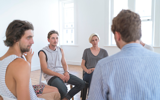 Men and women listening to therapist during meeting with a support group. Males and females are doing group therapy session. They are sharing ideas in bright room.