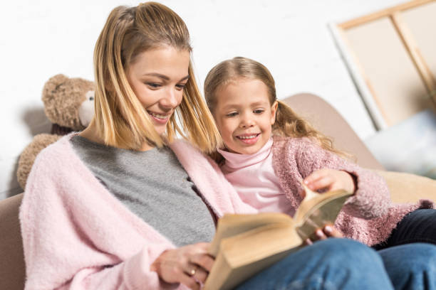 istock happy mother and daughter reading book together on sofa 923306002