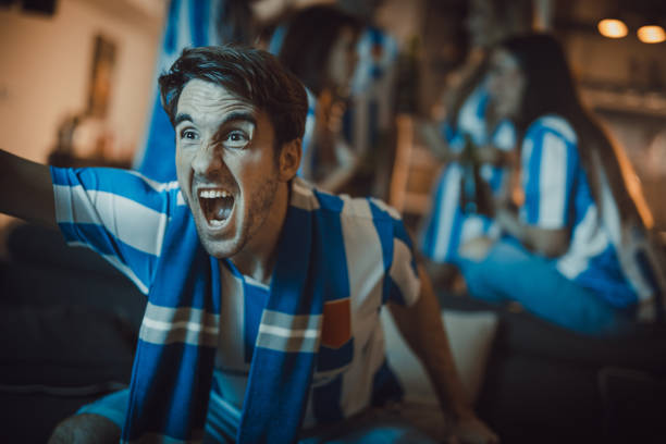 Young man encouraging his team while watching a match on TV at home.