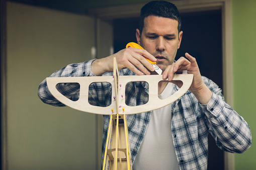 Mature man assembling parts of airplane in his workshop.