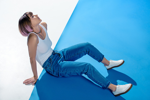 stylish girl sitting in shirt and jeans on white and blue floor